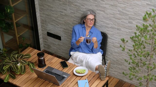 Stylish senior woman relaxing with a cup of coffee and breakfast on her modern balcony