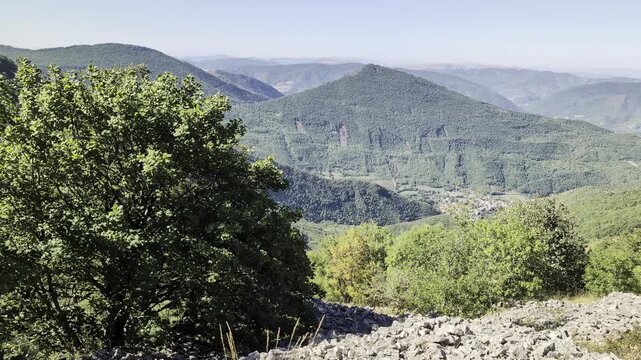 veduta panoramica dall'alto su una vallata di montagna con fitti boschi verdi, colline e rilievi montuosi sullo sfondo