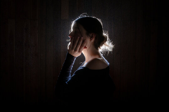 Backlit woman with hand to her cheek indoors