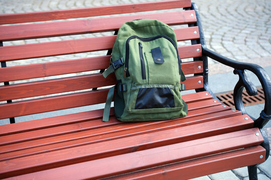 Green backpack sitting unattended on a public park bench, representing a forgotten personal item left in a city environment.