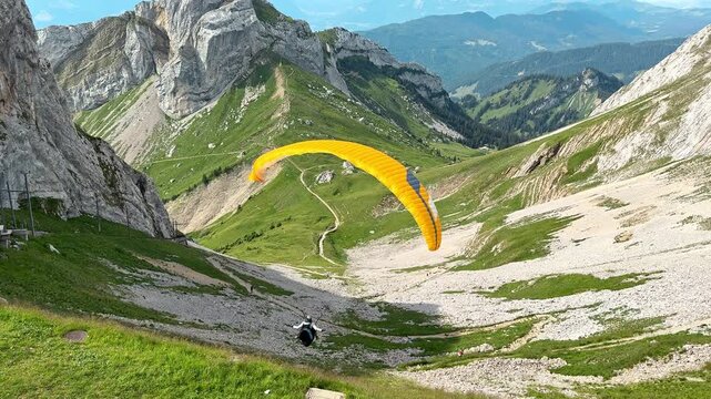 Yellow paraglider flies over green slopes beneath Mount Pilatus outdoors, Adventure footage captures free flight above a dramatic Swiss Alpine valley