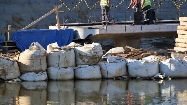 Construction workers building bridge over water with sandbags and reflections