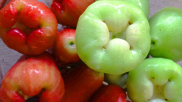 A close-up of freshly washed wax apples, also known as rose apples or water apples, placed in a metal strainer. The glossy red and green fruits highlight tropical freshness and vibrant natural colors