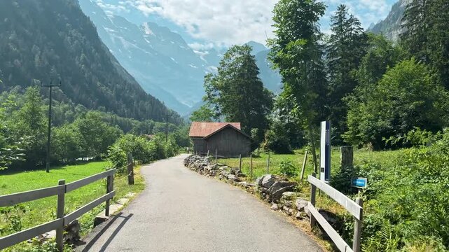 Empty paved path curves through green farmland in Lauterbrunnen outdoors, Swiss mountain cliffs and rustic barns frame a peaceful rural route outdoors