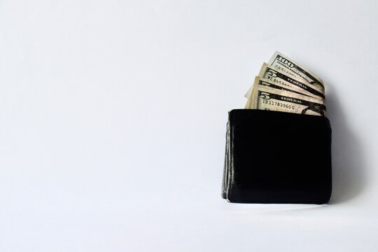 Black leather wallet with visible US dollar bills isolated on a clean white background.