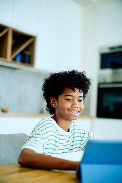Happy boy with braces smiling while using a digital tablet for remote learning and education in a modern kitchen