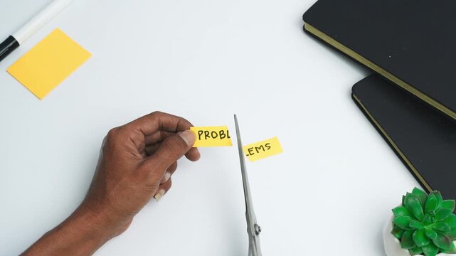 A Man is cutting a sticky note with the word PROBLEMS written on it using scissors. A concept of overcoming challenges.