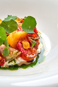Macro detail of gourmet salad with tomatoes, stracciatella, raspberries, and fresh herbs in white bowl.