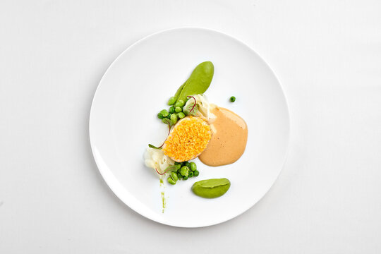 Top view of a gourmet fish fillet dish with green pea puree, creamy sauce, and edamame on a white plate, isolated on white background.