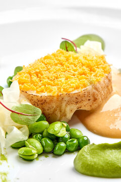Macro detail of a crust-topped fish fillet served with green pea puree, edamame, and sauce on a white plate.