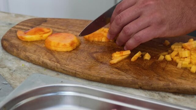 Close up of persons hands dicing fresh yellow peaches on wooden cutting board in kitchen