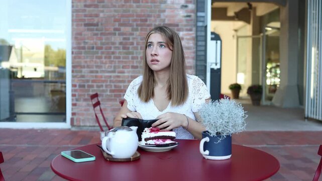 A young student discovers her wallet is empty and worries she cannot pay for food at a cafe reflecting financial stress rising prices and the growing cost of living today