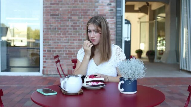 Distressed young woman holds her face at an outdoor cafe after finding her wallet empty and realizing she has no money to pay for cake and coffee causing financial stress
