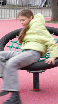 Young girl spinning fast on modern round playground carousel with net seat in outdoor park