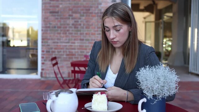 Food critic writes detailed notes after tasting cake and tea at an outdoor cafe documenting flavor quality service and overall dining experience carefully