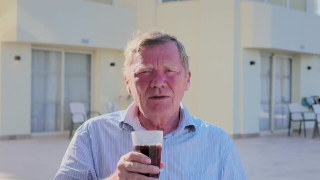 Sunburned senior man holding cold beverage in glass while relaxing outdoors