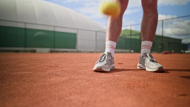 Cropped shot of unrecognizable young adult athlete bouncing tennis ball on ground before serving on outdoor clay court. Clip ideal for sports marketing, tennis coaching, and active lifestyle campaigns