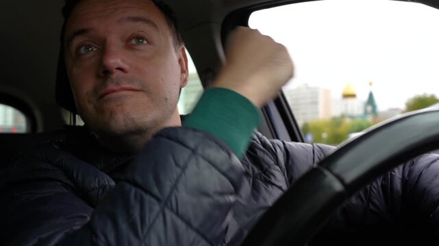 Focused mid-adult man in warm jacket driving car through city streets