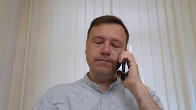 Serious adult man having phone call and gesturing while talking inside office