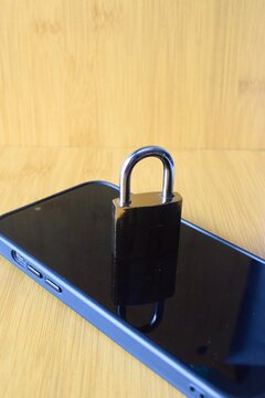 A metal padlock resting on a modern smartphone screen on a wooden surface, symbolizing mobile data security and privacy.