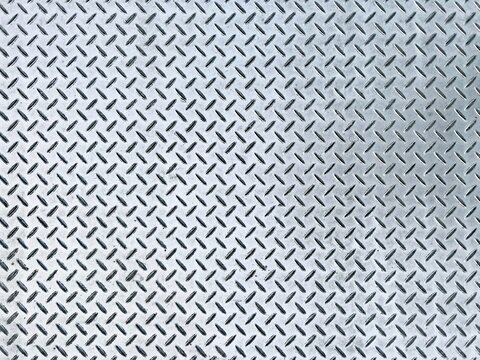 Top-down view of a shiny silver diamond plate steel metal texture with raised tread pattern for non-slip flooring.