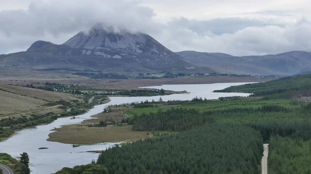 A scenic drone shot capturing the misty peak of Mount Errigal in Donegal, Ireland, overlooking a winding river and lush green woods. Ideal for travel and sustainability themes.