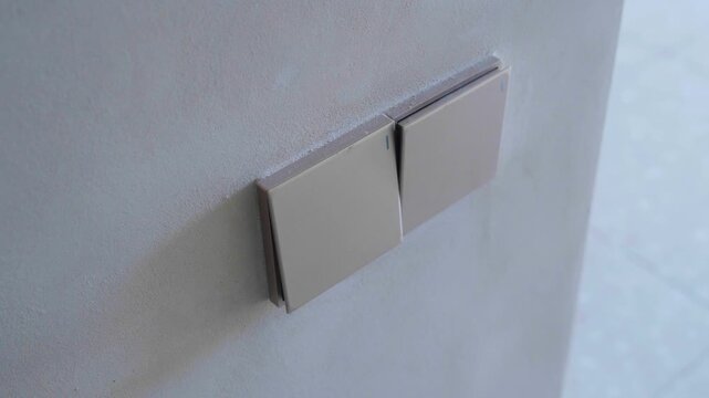 Close-up of two square rocker light switches mounted side by side on a light-colored wall. The neutral wall controls form a simple geometric detail in an indoor setting.