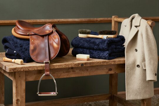 Leather saddle and coat arranged on wooden tack bench