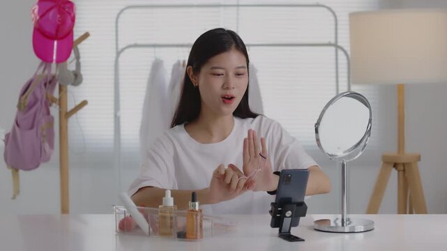 Young Asian beauty vlogger using an eyelash curler while recording makeup tutorial on smartphone.