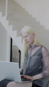 Slow motion of attractive albino girl using laptop computer sitting on stairs in creative luxury house. Businessperson and modern interior concept.