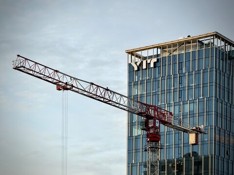 Low-angle photo of a red construction crane jib extending past a modern glass high-rise featuring the YIT corporate logo in Vilnius, Lithuania. Ideal for stock photo needs related to construction 