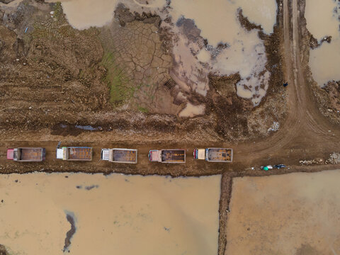 Trucks Waiting in Line on Muddy Off-Road Terrain at a Large-Scale Rock and Sand Quarry, Heavy Mining Vehicles Support Active Construction and Raw Material Extraction Operations view from above.