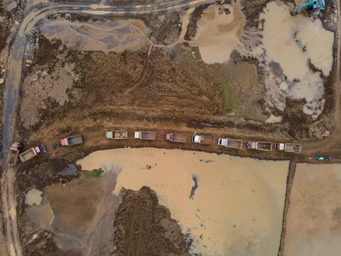 Trucks Waiting in Line on Muddy Off-Road Terrain at a Large-Scale Rock and Sand Quarry, Heavy Mining Vehicles Support Active Construction and Raw Material Extraction Operations view from above.