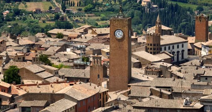 Aerial view of Torre del Moro rising above the terracotta rooftops of Orvieto, in the province of Terni, Umbria, Italy, with green hills visible in the background. It's a summer morning.