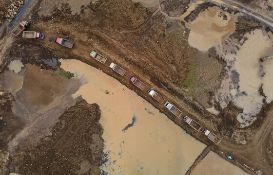 Trucks Waiting in Line on Muddy Off-Road Terrain at a Large-Scale Rock and Sand Quarry, Heavy Mining Vehicles Support Active Construction and Raw Material Extraction Operations view from above.