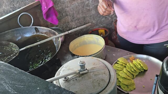 Indian Street Food Chef Using Slotted Skimmer Spoon to Remove Crispy Fried Gram Flour Batter Droppings from Hot Oil Wok During Fresh Vada Pav Preparation at Open Outdoor Kitchen Stall