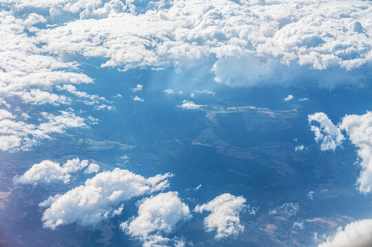 Aerial view of green rural landscape and fields seen through fluffy white clouds
