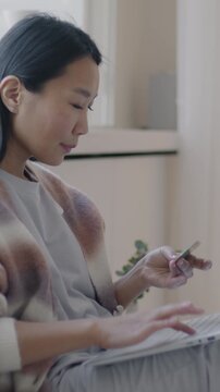 Slow motion of gorgeous Asian lady shopping online with laptop and credit card sitting in bed in luxury bedroom. Consumerism and banking concept.