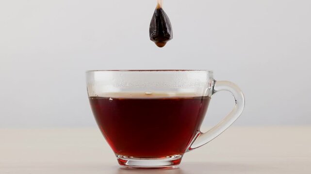 Dipping Tea Bag into Glass Cup of Hot Black Tea