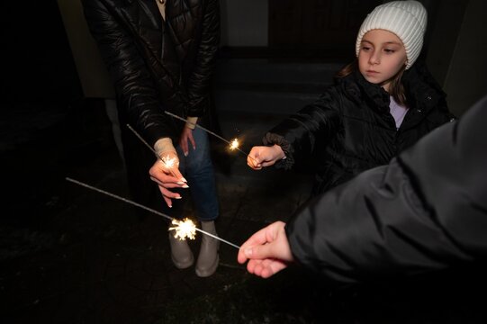 Child and adult celebrating together with sparklers under a starlit sky during a festive nighttime gathering in a cozy neighborhood setting