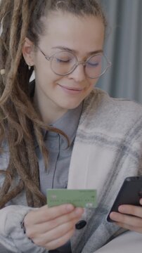 Cheerful young lady shopping online paying with credit card using smartphone indoors in luxury apartment. Banking and consumerism concept.
