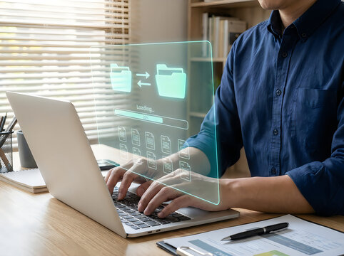 Person in a blue shirt typing on a laptop with a digital holographic loading bar and folder representing file transfer and data management
