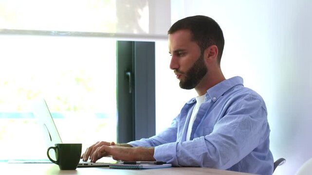 Exhausted caucasian freelancer working on his laptop from home and feeling neck pain due to bad posture, massaging his tense muscle to relieve the discomfort from a sedentary lifestyle