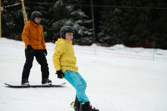 Excitement on the slopes as a child learns snowboarding from an experienced mentor during a winter afternoon in a scenic snowy landscape