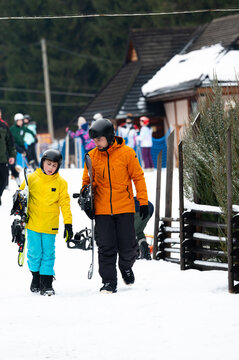 Father and son enjoy a snowy day while heading to the ski slopes in a vibrant winter wonderland filled with excited skiers in the background during the holiday season