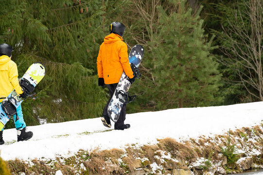 Snowboard enthusiasts trek through snowy terrain toward the slopes in a vibrant winter landscape surrounded by evergreens and mountain beauty