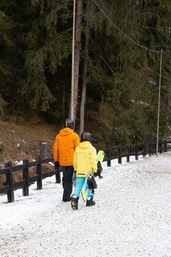 Adventurous duo walking through snowy trails in winter wonderland as they prepare for an exciting day of snowboarding in the mountainous landscape surrounded by tall trees