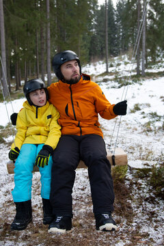 Enjoying a winter day in the forest with family while swinging on a wooden swing amidst snow and trees in a cozy atmosphere