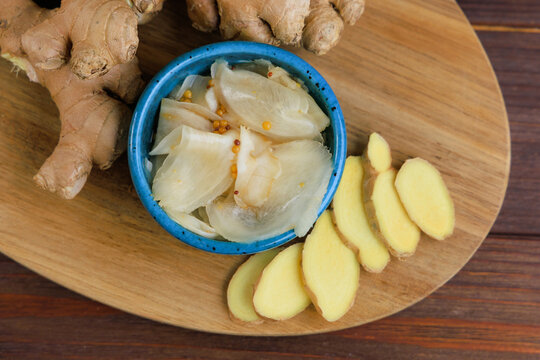 Pickled ginger in a blue bowl with fresh ginger on a wooden plate
