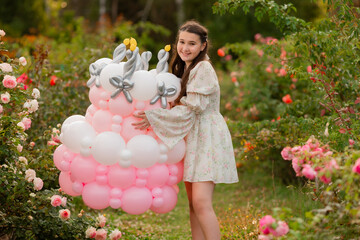 Fototapeta premium A girl in a rose garden, wearing a romantic dress, is holding a marshmallow cake and blowing out the birthday candles.